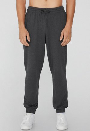 Graue Jogginghosen mit Kordelzug und elastischen Bündchen, aus weichem Stoff hergestellt. Sie haben eine schmale Passform und werden mit weißen Sneakern getragen. Keine Muster oder Verzierungen.