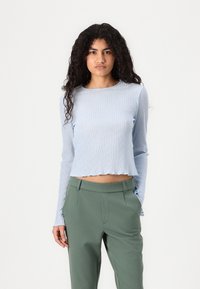 Světle modrý žebrovaný dlouhý rukáv crop top s vlnitým lemem, spárovaný se zelenými kalhotami s pohodlným střihem a bočními kapsami.