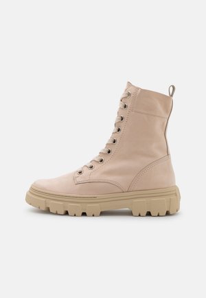 Beige nahkasaappaat nilkkapituisuudella, joissa on kumipohja, kuusi reikää kengännauhoille ja vetotanko. Sileä pinta, vahvistetut saumat ja muotoilultaan jämäkkä.