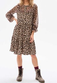 Robe à imprimé léopard avec un col à volants et des manches longues transparentes, dotée d'une jupe à volants et assortie à des bottes au même motif.