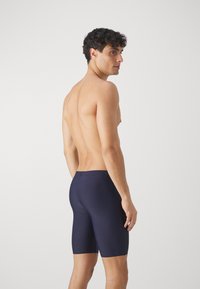 Mørkeblå badetights laget av glatt materiale, med en tettsittende design som går til midten av låret. Minimalistisk stil uten mønstre.