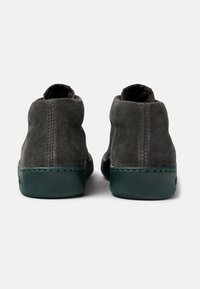 Šedé semišové kotníkové boty s hladkou tmavozelenou gumovou podrážkou. Zaoblená špička a minimalistický design s detailním prošíváním na zadní straně.