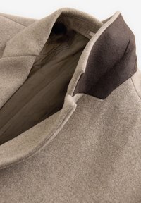 Beige wool blend coat with a dark brown collar, featuring a textured exterior and smooth inner lining. Notable tailored lapels.