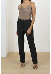 Satiinihihna taupe-värissä pitsiyksityiskohdilla, yhdistetty mustiin mittatilaustyönä tehtyihin housuihin. Mallilla on myös mustat nilkkaketjuhatut. Yksinkertainen ja tyylikäs muotoilu.