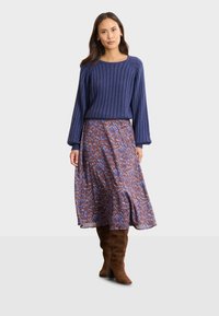 Lila ribbad tröja i kombination med en mönstrad midilång kjol i blå, röd och bruna nyanser. Modell som bär bruna knähöga stövlar.