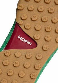 Suela de zapatilla verde con una base de goma marrón texturizada y patrones hexagonales, un acento rojo y el nombre de la marca "HOFF" en blanco.