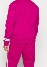 Sudadera fucsia con rayas blancas en los puños y pantalones a juego. Hecha de tela suave y lisa. Diseño sencillo y relajado.