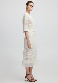 Zweiteiliges Strickoutfit in hellem Beige, mit horizontalen Streifen und offenen Geweben; kombiniert mit braunen Riemchensandalen.