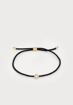 Bracelet tressé noir avec un accent doré et une pierre claire circulaire au centre. Fins cordons réglables avec des embouts dorés.