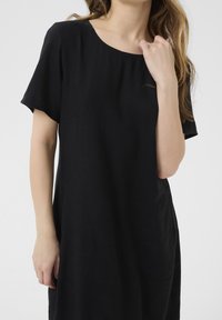 Schwarzes Kurzarmkleid mit rundem Halsauschnitt, aus leichtem Stoff. Verfügt über dezente Seitentaschen und eine lockere Passform.