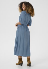 Blå, långärmad klänning med bälte i midjan, lös passform och sidfickor. Bärs med bruna, klackiga, mocka ankelskorr.