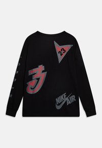 Svart långärmad tröja med grafiska element: röd triangel med "23," stiliserad röd pil och Nike Air-logotyp i grått över ryggen.