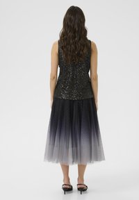 Top de lentejuelas negras con un diseño ajustado y una falda de tul fluida en ombré que va de gris oscuro a claro, adornada con sutiles destellos.