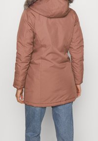 Brązowy ocieplany płaszcz z futrzanym kapturem, z prostym krojem, długimi rękawami i gładką fakturą. Widok z tyłu.