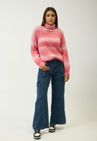 Roze en witte gestreepte gebreide trui met een hoge kraag, gecombineerd met brede blauwe denim cargobroek met zakken en een rafelige zoom.