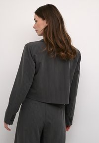 Grå pinstribet blazer med en cropped ryg, der har lange ærmer og knapdetaljer ved manchetterne. Stoffet ser glat ud med et struktureret design.