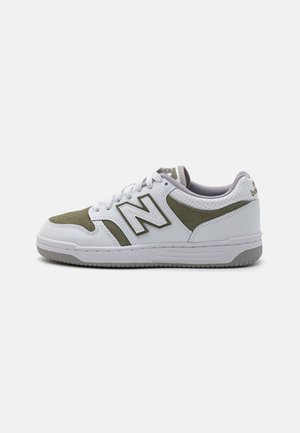 Baskets blanches et vert olive avec fermeture à lacets, talon perforé et logo "N" bien visible sur le côté, affichées sur un fond uni.