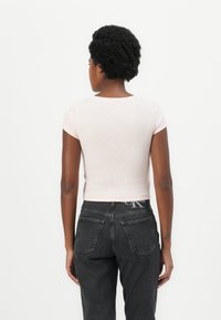 Crop top aderente a maniche corte in morbido tessuto a coste di un delicato rosa pastello, abbinato a jeans neri in denim a vita alta con tasche posteriori.