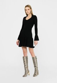 Robe en maille noire avec des manches longues évasées et un ourlet évasé. Associée à des bottes brillantes montant jusqu'aux genoux avec un motif serpent.