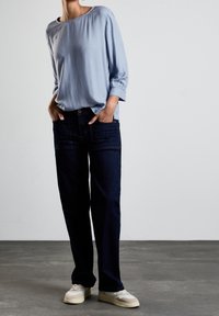 Ljusblå, långärmad blus i löst snitt, tillsammans med mörkblå raka jeans. Sneakers har grädd- och beige detaljer.