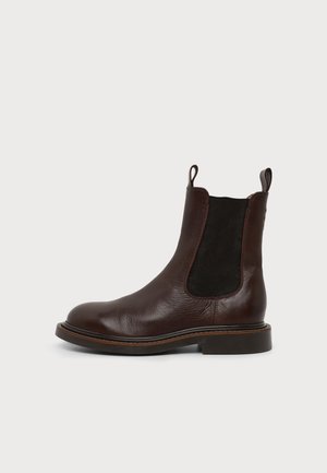 Bottine en cuir marron foncé avec empiècement élastique noir sur les côtés et languettes sur fond blanc.