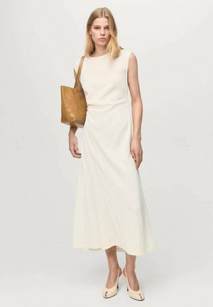 Vestido largo sin mangas color marfil con corte recto y una textura sutil. Combinado con un bolso tote de cuero color marrón claro y mules de tacón en tonos claros.