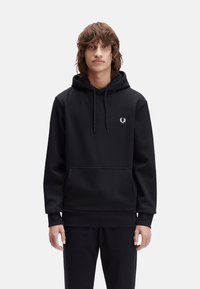 Sudadera negra con capucha, hecha de tejido grueso, que cuenta con un bolsillo frontal, cordones ajustables y un pequeño logo blanco en el pecho.