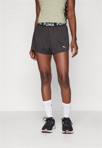 Mustad sportlikud lühikesed püksid, millel on PUMA logo vöö, koos valgete sokkidega ja mustade jooksumudelitega, millel on roosa aktsent.