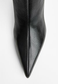 Bottines noires à talon pointu en cuir synthétique texturé. Finition lisse avec une silhouette épurée et une couture centrale.