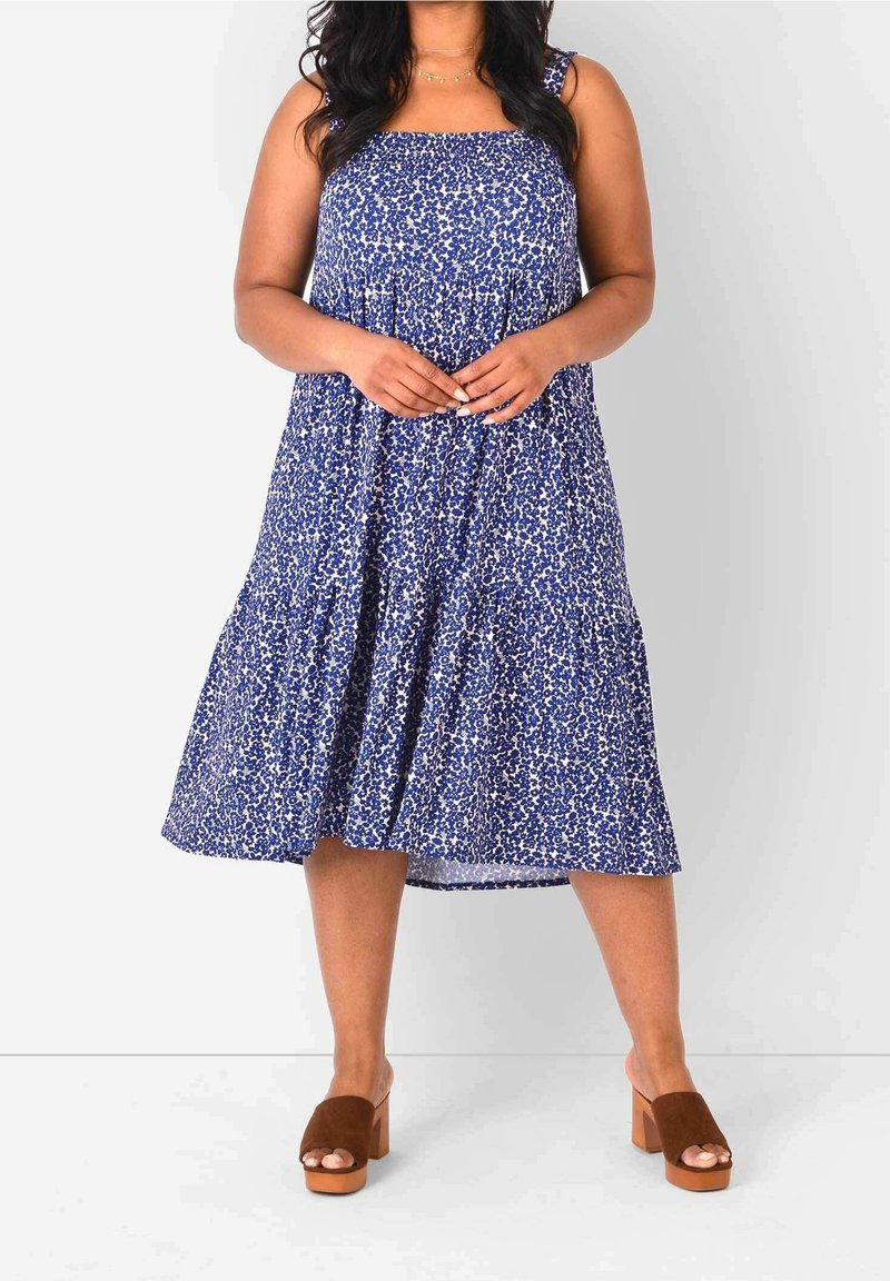 Blaue Blumen-Midi-Kleid mit einem quadratischen Ausschnitt, breiten Trägern und gerafftem Oberteil. Kombiniert mit braunen Absatzsandalen.