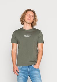 Olivengrøn bomulds t-shirt med korte ærmer, der har et hvidt logo print på brystet og et lille mærke på ærmet.