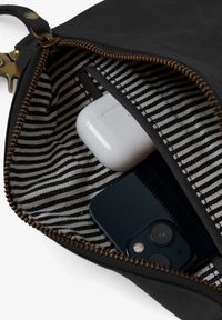 Black zippered pouch with striped interior lining holding white wireless earbuds case and black smartphone camera visible.