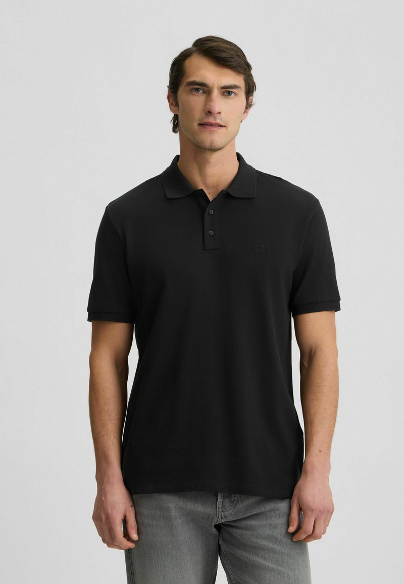 Polo shirt nera a maniche corte con colletto, dotata di tre bottoni e di un accento logo discreto sul petto. Tessuto morbido e liscio.