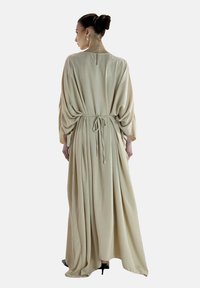 Robe longue beige en tissu doux, avec une taille à nouer, des manches larges et une texture subtile, dotée d'un détail en trou de serrure au dos.