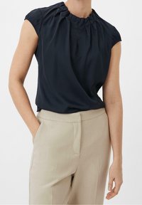 Blusa blu navy con scollatura arricciata e maniche corte, abbinata a pantaloni beige chiaro su misura. Tessuto morbido al tatto e vestibilità rilassata.