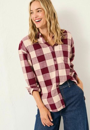 Burgundy and cream checkered button-up shirt with a collar, rolled sleeves, and single chest pocket, paired with blue denim pants.