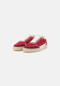 Sneakers in suede rosso con dettagli in pelle bianca, lacci piatti e suola in gomma crema. Presentano dettagli di cucitura e un design minimalista.