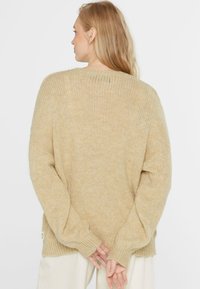 Beige übergroßer Strickpullover mit lockerer Passform, gerippten Bündchen und strukturierter Oberfläche. Der Rücken zeigt einen weiten Ausschnitt und subtile Nahtdetails.