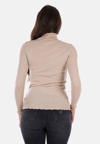 Top a maniche lunghe a coste beige con colletto alto e orlo ondulato, caratterizzato da una leggera lucentezza e una silhouette aderente. Vista posteriore mostrata.