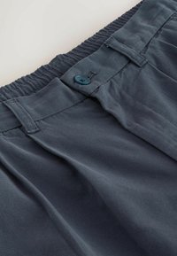 Pantalon en tissu gris foncé texturé avec ceinture élastique, fermeture par bouton, passants pour ceinture et plis à l'avant.