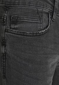 Mustat farkut, joissa on takatasku, siistit linjat, hillitty ommel ja teksturoidun näköinen pinta. Taskussa on napitus.