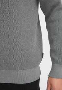 Maglione grigio a maglia con un motivo a punto testurizzato, polsini e orlo a coste, con una piccola etichetta del marchio sul lato.