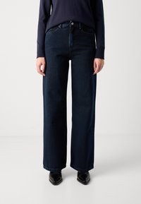 Wijde donkerdenim jeans met een schone afwerking, hoge taille en vijf zakken. Gepaard met een marineblauw langemouwen T-shirt en zwarte schoenen.