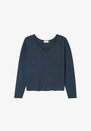 Tumši zila auduma krekls ar garām piedurknēm un V-veida kakla izgriezumu. Tam ir brīvs griezums ar nedaudz saīsinātu apakšmalu un tekstūras variācijām. Nav redzamu detaļu.