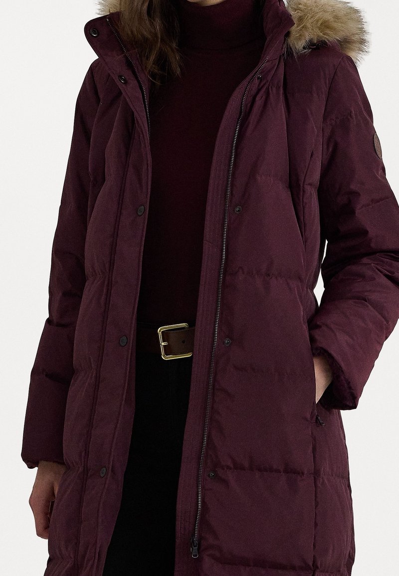 Burgundské péřové sako se zipem a patentním uzávěrem, vybavené kapucí podšitou umělou kožešinou. Látka má hladký, matný povrch a je prošívaná.
