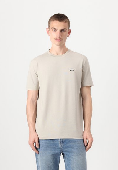 T-shirt beige à manches courtes avec col rond, affichant un petit logo noir "BOSS" sur la partie gauche de la poitrine. Texture lisse, coupe décontractée.