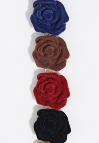 Akcesorium w kształcie róży z aksamitnej tkaniny, z ciemnoniebieskimi, brązowymi, czerwonymi i czarnymi kwiatami, połączonymi złotą pierścionkiem. Miękka tekstura i warstwowy design.