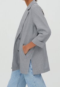 Black and white checkered blazer with a loose fit, notch lapels, and two side pockets. The fabric has a smooth texture and a slightly structured design.