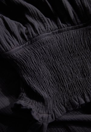 Tissu noir texturé avec des plis verticaux, présentant des bords froncés. Matériau doux avec un léger éclat et une finition lisse.