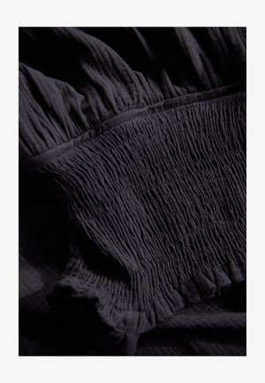 Schwarzer Strukturstoff mit vertikalen Falten und gerafften Kanten. Weiches Material mit leichtem Glanz und glatter Oberfläche.